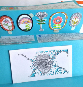 Hand written letter on white pieces of paper glued over rich blue paper, it has a row of hand painted whimsical flower stickers and a paper cut out in progress